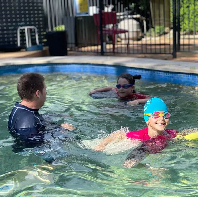 Coach teaching a child to swim in a backyard pool